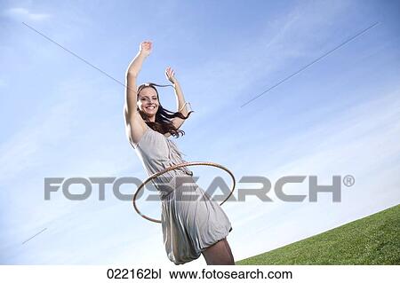 Stock Image - young woman in park doing hula hoop. Fotosearch