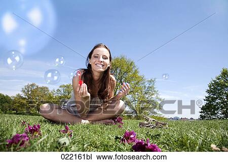 young woman sitting in grass blowing soap bubbles View Large Photo Image Stock Image - young woman sitting in grass blowing soap bubbles. Fotosearch