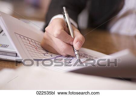 Stock Image - detail of young businesswoman sitting at desk writing graph in document. Fotosearch