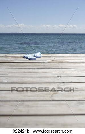 Stock Image - pair of flip flops on wooden pier in front of the ocean. Fotosearch