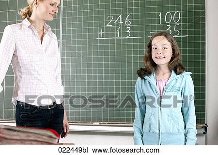 Stock Image - teacher and young girl in front of blackboard in classroom. Fotosearch