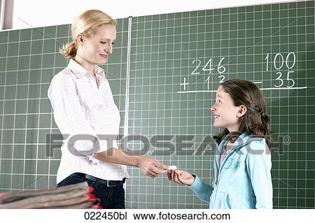 Stock Image - teacher and young girl in front of blackboard in classroom. Fotosearch