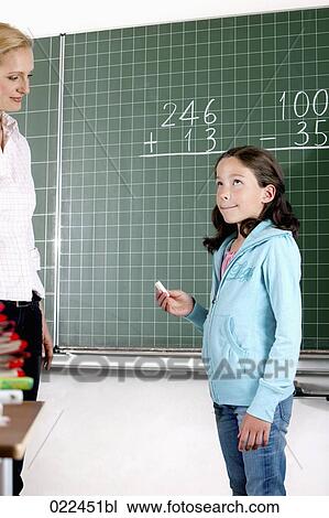 Stock Image - teacher and young girl in front of blackboard in classroom. Fotosearch