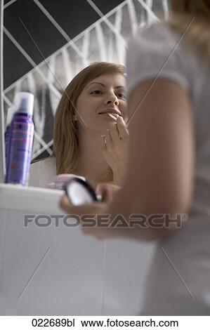 Stock Image - young woman in front of mirror applying lipstick. Fotosearch