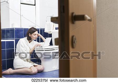 Stock Image - young woman with laptop computer in bathroom. Fotosearch