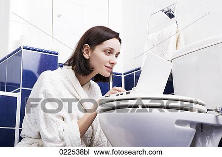 Stock Image - young woman with laptop computer in bathroom. Fotosearch