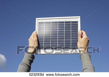 Stock Image - detail of woman holding solar panel up against sky. Fotosearch