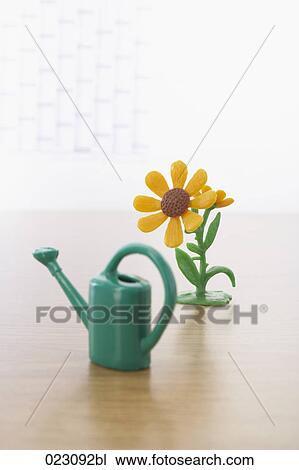 Stock Image - miniature of watering can and sunflower on table. Fotosearch