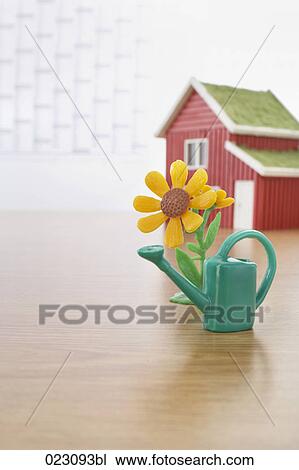 Stock Image - miniature of watering can and sunflower on table. Fotosearch