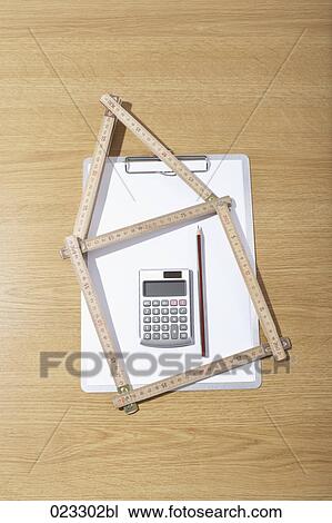 Stock Image - still life of folding rule in shape of house clipboard and calculator. Fotosearch