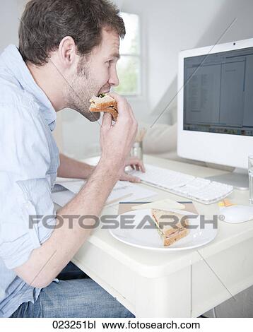 young man at desk eating sandwich and working with computer View Large Photo Image Stock Image - young man at desk eating sandwich and working with computer. Fotosearch