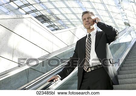 businessman standing on escalator talking on mobile phone View Large Photo Image Stock Image - businessman standing on escalator talking on mobile phone. Fotosearch