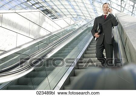 businessman walking down escalator and talking on mobile phone View Large Photo Image Stock Image - businessman walking down escalator and talking on mobile phone . Fotosearch
