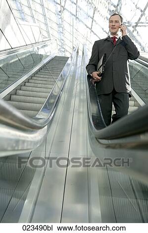 businessman walking down escalator and talking on mobile phone View Large Photo Image Stock Image - businessman walking down escalator and talking on mobile phone . Fotosearch