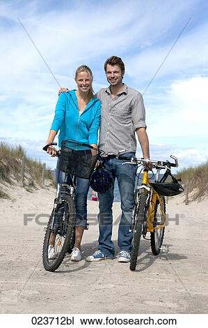 Stock Image - portrait of young couple with bicycles on the beach. Fotosearch