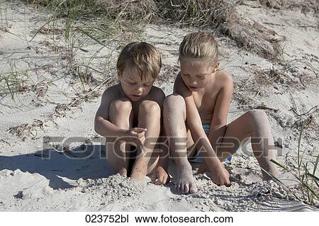 Stock Image - sister and brother sitting together in sand. Fotosearch