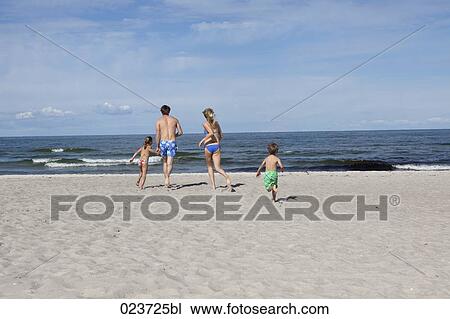 Stock Image - young family on beach running towards the sea. Fotosearch