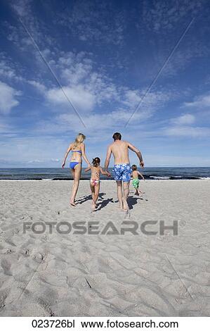 Stock Image - young family on beach running towards the sea. Fotosearch