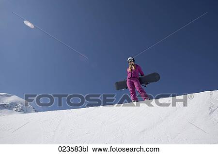 Stock Image - young woman in mountains holding snowboard. Fotosearch