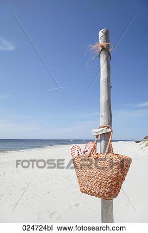 Stock Image - basket with flip flops hanging on pole at beach. Fotosearch