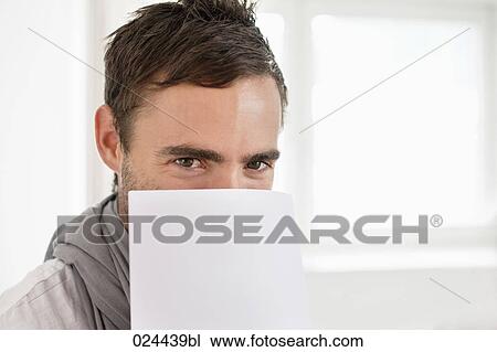 Stock Image - headshot of young man hiding behind document. Fotosearch