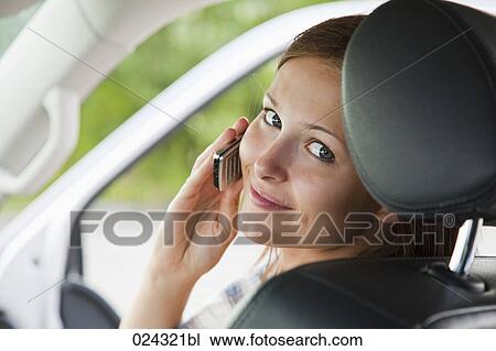 Stock Image - headshot of young woman in car talking on mobile phone. Fotosearch