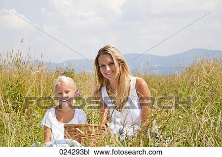 Stock Image - mother and young daughter sitting in meadow. Fotosearch
