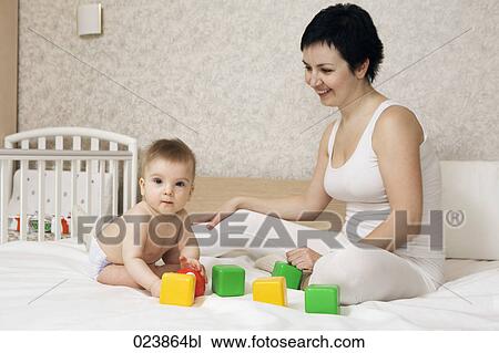 Stock Image - mother watching her baby boy play on bed. Fotosearch