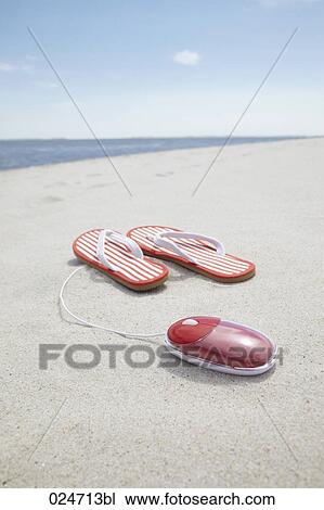 Stock Image - pair of flip flops and computer mouse on sandy beach. Fotosearch