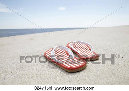 Stock Image - pair of flip flos on sandy beach. Fotosearch