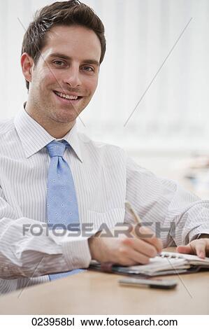 Stock Image - portrait of young businessman at desk with diary. Fotosearch