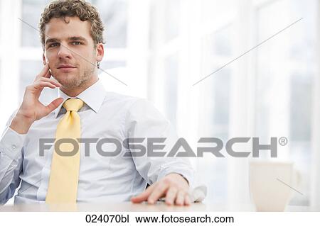 Stock Image - portrait of young businessman sitting at desk. Fotosearch