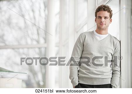 Stock Image - portrait of young businessman standing by a window. Fotosearch