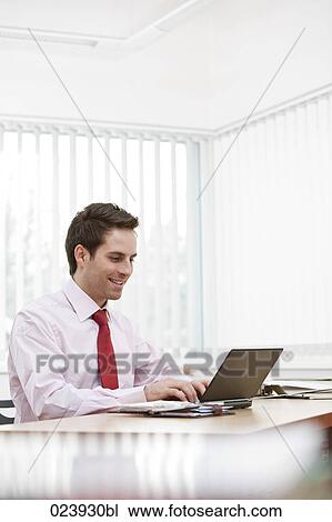 Stock Image - portrait of young businessman working with laptop computer. Fotosearch