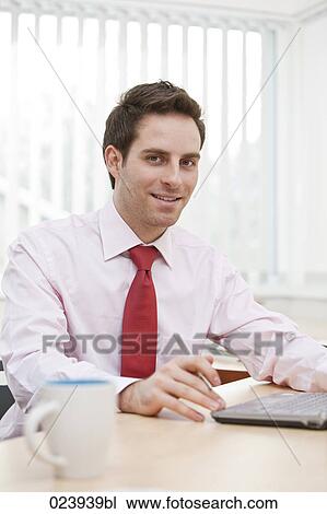 Stock Image - portrait of young businessman working with laptop computer. Fotosearch