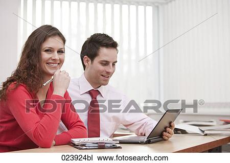 Stock Image - portrait of young businesswoman and male colleague sitting at desk. Fotosearch