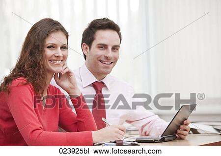 Stock Image - portrait of young businesswoman and male colleague sitting at desk. Fotosearch