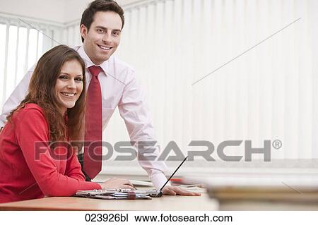 Stock Image - portrait of young businesswoman and male colleague sitting at desk. Fotosearch
