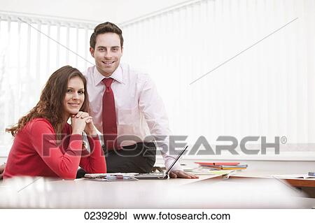 Stock Image - portrait of young businesswoman and male colleague sitting at desk. Fotosearch