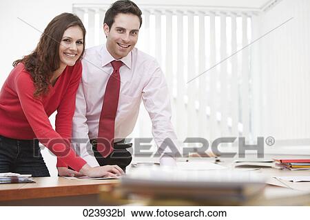 Stock Image - portrait of young businesswoman and male colleague sitting at desk. Fotosearch