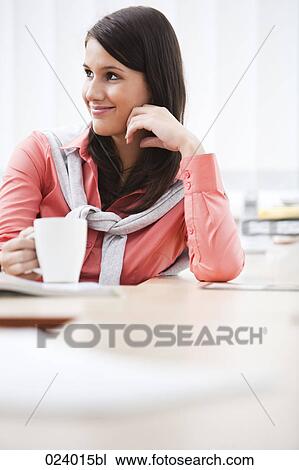 Stock Image - portrait of young businesswoman sitting at desk with cup. Fotosearch