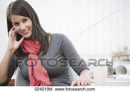 Stock Image - portrait of young businesswoman sitting at desk with cup. Fotosearch