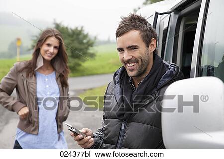 Stock Image - portrait of young couple at car man with mobile phone. Fotosearch