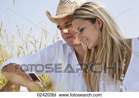 portrait of young couple in meadow reading text message on mobile phone View Large Photo Image Stock Image - portrait of young couple in meadow reading text message on mobile phone. Fotosearch