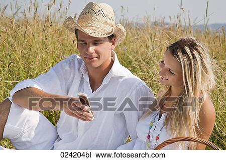 portrait of young couple in meadow reading text message on mobile phone View Large Photo Image Stock Image - portrait of young couple in meadow reading text message on mobile phone. Fotosearch