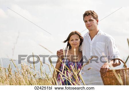 Stock Image - portrait of young couple with picnic basket in field. Fotosearch