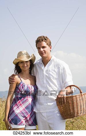 Stock Image - portrait of young couple with picnic basket in field. Fotosearch