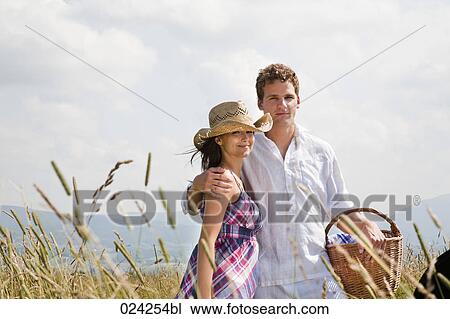 Stock Image - portrait of young couple with picnic basket in field. Fotosearch
