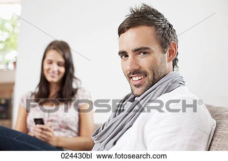 Stock Image - portrait of young man at home with girlfriend in background. Fotosearch