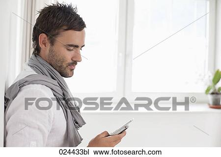 Stock Image - portrait of young man in empty room with mobile phone. Fotosearch